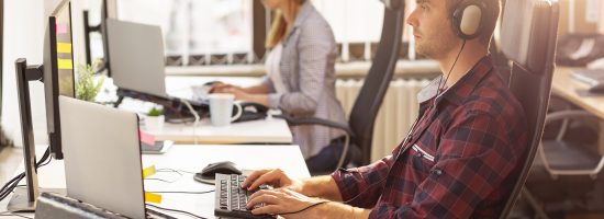 IT support team working in an office; call centre operators wearing headsets and typing on a computer keyboard, receiving calls