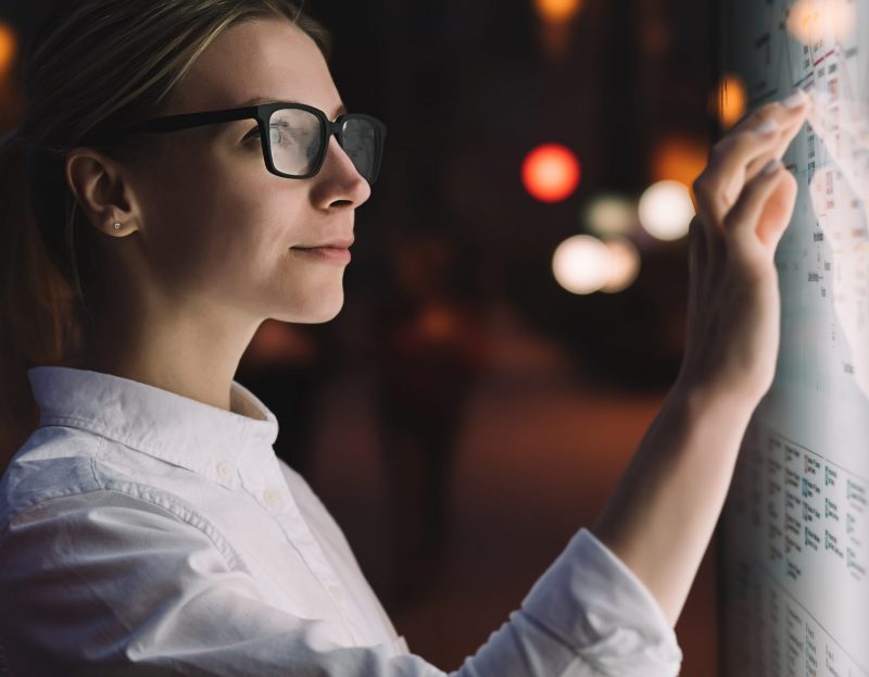 Digital monitor with public transport subway map. Female standing at big display with advanced innovative technology. Young woman touching with finger sensitive screen while selecting surface option